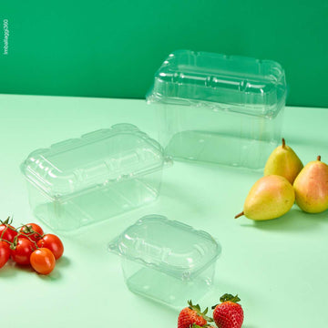 Vaschetta trasparente per frutta e verdura, varie misure e vuote, su sfondo verde, con accanto pere, fragole e pomodorini